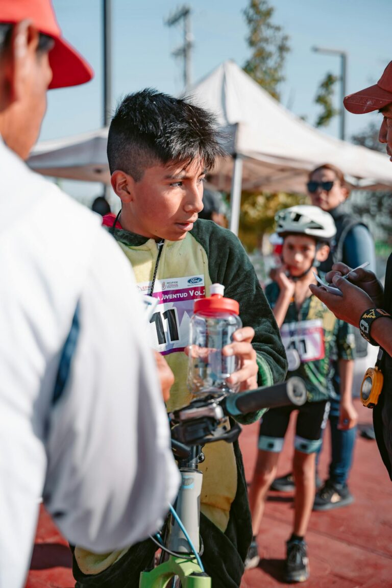 A young cyclist takes a break with a water bottle after participating in a track event.